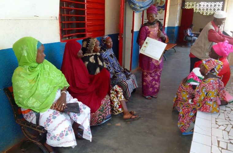 Séance de sensibilisation dans la salle d’attente d’un centre de santé : une animatrice présente une boîte à images à des femmes assises.